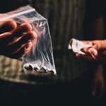 Photo of hands holding a baggie of pills and cash